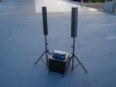 A pair of column-array speakers on stands flanking a subwoofer and a rack-mounted digital mixer at dusk
